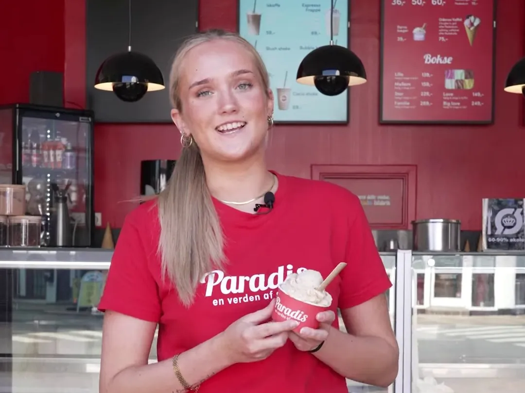 Smilende Paradis-medarbejder i rød T-shirt med en bæger is i butikken